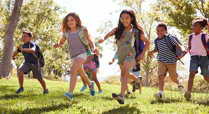 A group of children run in a field carrying backpacks