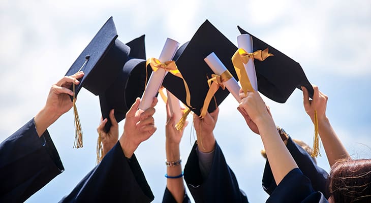 Graduates hold up their caps and diplomas on a sunny day