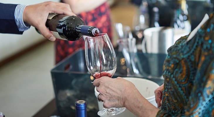 a server pours a glass of red wine at a festival