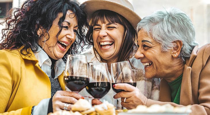 three friends laugh and toast glasses of wine