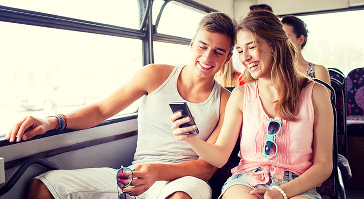 tourists smile at their phones on a tour bus